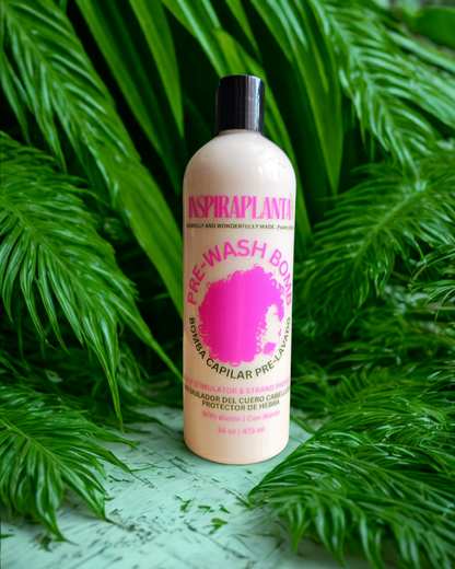 INSPIRAPLANTA 16 oz Pre-Wash Bomb bottle with pink label in front of vibrant green tropical leaves.